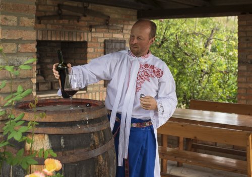 Vinař Martin Bravenec začal dosahovat úspěchů už po pár letech. Vinař Martin Bravenec se dívá na lahev s červeným vínem a skleničku položenou na dřevěném sudu.